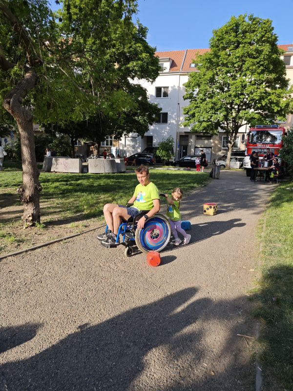 Tatínek sedí na vozíku, který veze jeho malá dcera a společně projíždějí slalom na Dni rodiny v Brně-Židenicích