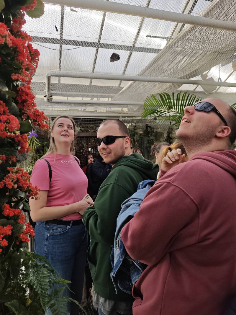 asistentka a dvojice účastníků poznávacího kroužku ve skleníku na výstavě motýlů