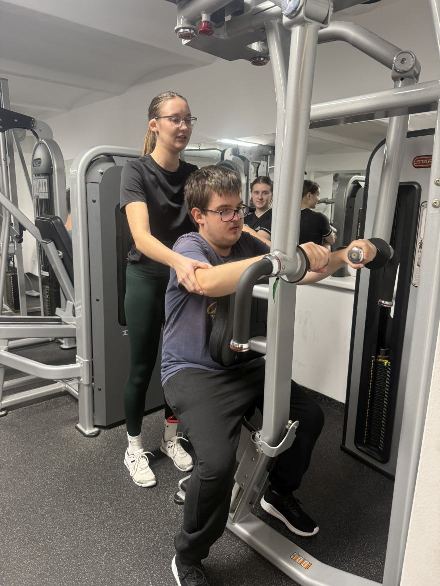 asistentka pomáhá klientovi s cvičením na stroji na fitness víkendu